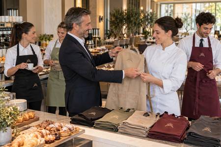 Consegna di grembiuli personalizzati al personale di un hotel con un simbolo coordinato.